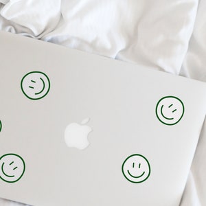 May include: A silver laptop computer with five green smiley face stickers on the lid.