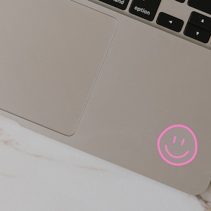 May include: A pink smiley face sticker on a silver laptop.