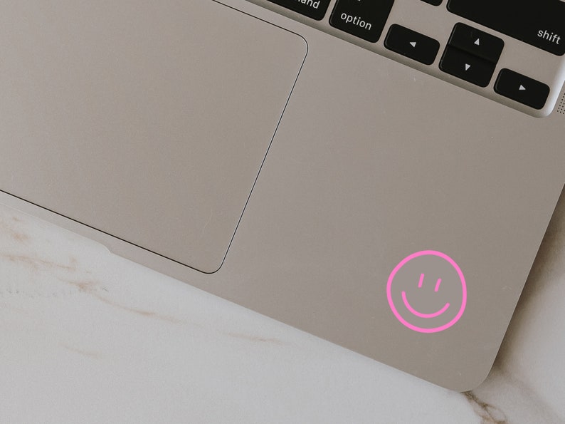 May include: A pink smiley face sticker on a silver laptop.