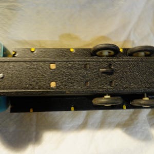 Pode incluir: Um caminh&atilde;o de brinquedo preto com uma cabine azul e detalhes amarelos. O caminh&atilde;o tem quatro rodas pretas com pneus brancos e uma plataforma.