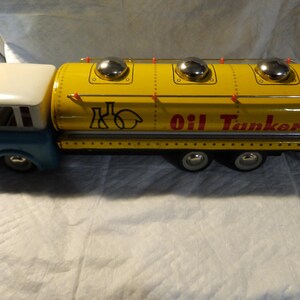 Pode incluir: Um caminh&atilde;o-tanque de &oacute;leo de brinquedo amarelo com uma cabine azul e um teto branco. O caminh&atilde;o tem tr&ecirc;s tampas prateadas no topo do tanque e as palavras "Oil Tanker" impressas no lado.