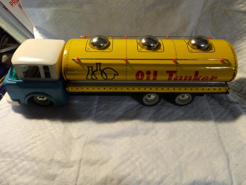 Pode incluir: Um caminh&atilde;o-tanque de &oacute;leo de brinquedo amarelo com uma cabine azul e um teto branco. O caminh&atilde;o tem tr&ecirc;s tampas prateadas no topo do tanque e as palavras "Oil Tanker" impressas no lado.