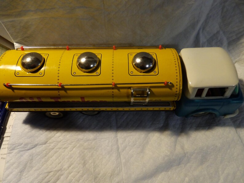 Pode incluir: Um caminh&atilde;o de brinquedo amarelo com uma cabine azul e um grande tanque amarelo. O tanque tem tr&ecirc;s detalhes circulares prateados no topo. O caminh&atilde;o &eacute; de metal e tem um visual vintage.
