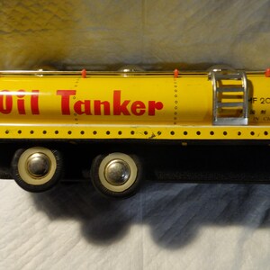 Pode incluir: Caminh&atilde;o-tanque de &oacute;leo de brinquedo amarelo com rodas pretas e uma escada no lado. O tanque tem "Oil Tanker" impresso em letras vermelhas e "MF 201 Made in China" impresso em letras pretas.