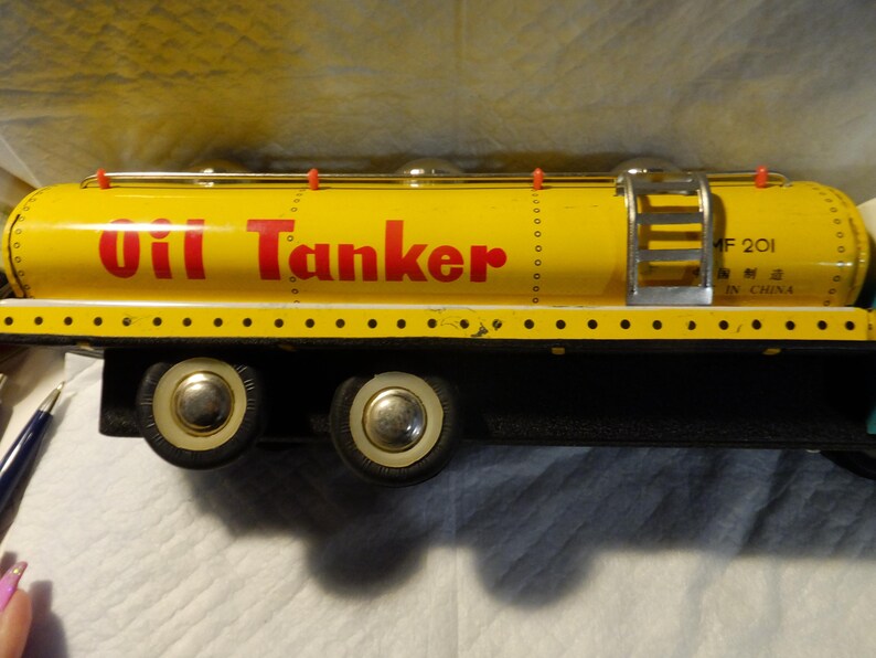 Pode incluir: Caminh&atilde;o-tanque de &oacute;leo de brinquedo amarelo com rodas pretas e uma escada no lado. O tanque tem "Oil Tanker" impresso em letras vermelhas e "MF 201 Made in China" impresso em letras pretas.