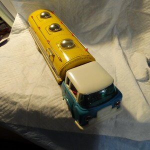 Pode incluir: Um caminh&atilde;o de brinquedo vintage com um tanque amarelo e uma cabine azul. O tanque tem tr&ecirc;s tampas prateadas no topo. O caminh&atilde;o &eacute; de metal e tem um telhado branco.