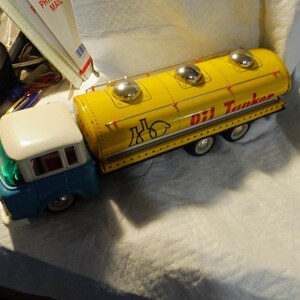 Pode incluir: Um caminh&atilde;o de brinquedo amarelo com uma cabine azul e um telhado branco. O caminh&atilde;o tem um grande tanque amarelo com as palavras "Oil Tanker" impressas no lado. O tanque tem tr&ecirc;s tampas prateadas no topo.