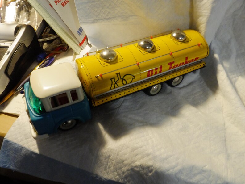 Pode incluir: Um caminh&atilde;o de brinquedo amarelo com uma cabine azul e um telhado branco. O caminh&atilde;o tem um grande tanque amarelo com as palavras "Oil Tanker" impressas no lado. O tanque tem tr&ecirc;s tampas prateadas no topo.