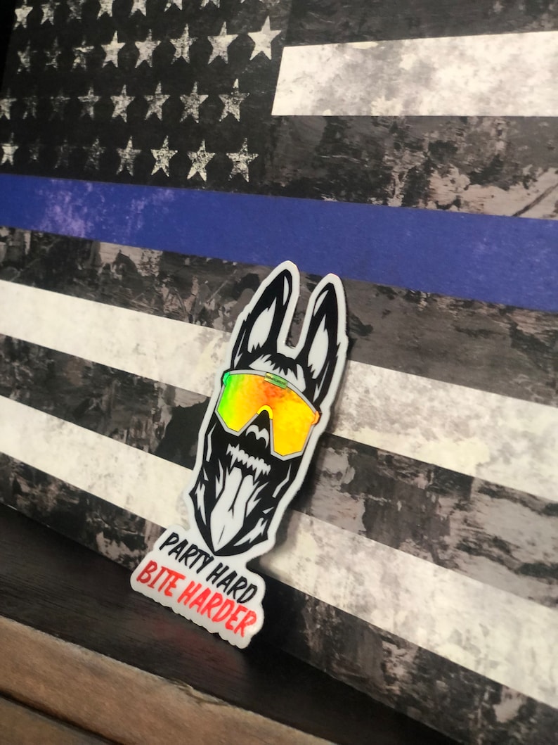 K&ouml;nnte beinhalten: Ein schwarz-wei&szlig;er Aufkleber eines Hundes, der eine Sonnenbrille mit Regenbogen-Schimmer tr&auml;gt. Die Zunge des Hundes h&auml;ngt heraus. Der Aufkleber tr&auml;gt den Text "Party Hard Bite Harder". Der Aufkleber befindet sich auf einem Hintergrund einer abgenutzten amerikanischen Flagge mit einem blauen Streifen.