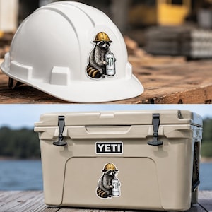 May include: A white hard hat and a tan cooler, each featuring a sticker of a raccoon wearing a yellow construction helmet and holding a silver can with the text Monster Energy. The raccoon is depicted in a seated position with a striped tail.