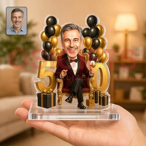 May include: A custom acrylic tabletop display featuring a caricature of a man in a maroon suit sitting on a gold chair, holding a glass. The design includes large gold number 50, black and gold balloons, and gift boxes on a clear base.