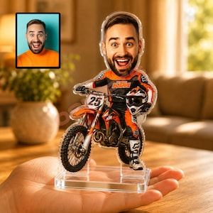 May include: A custom acrylic figurine featuring a caricature of a man with a beard, wearing orange and black motocross gear, sitting on an orange KTM dirt bike with the number 25. The figure is mounted on a clear rectangular acrylic base.