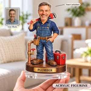 May include: A custom acrylic figurine of a smiling plumber wearing blue denim overalls and a shirt, holding a red pipe wrench. The figure stands on a wooden base with a gold plaque labeled PLUMBER, featuring a red toolbox and copper pipes.