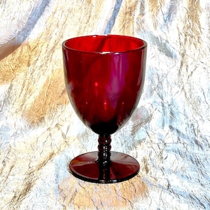 May include: A deep red glass goblet with a thick, round base and a stemmed design. The goblet is made of clear glass with a deep red hue.