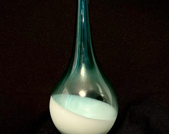 May include: A teardrop-shaped glass vase with a long, slender neck. The top half is a teal color, while the bottom half is white. The vase has a smooth, glossy finish and is likely used for decorative purposes.