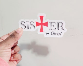 May include: White sticker with the words "Sister in Christ" in black text. A red cross is between the words "Sister" and "in".