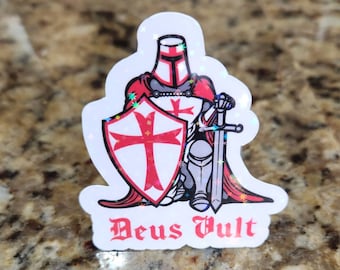 May include: A sticker featuring a knight in red and silver armor, holding a sword and shield with a red cross. The sticker has the words "Deus Vult" in a gothic font.