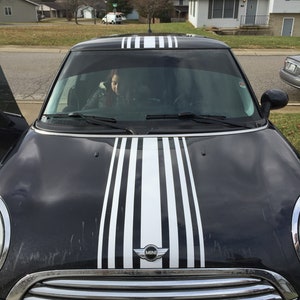 May include: A black Mini Cooper with white racing stripes down the bonnet. The car has a chrome grille and the Mini logo is visible on the front.