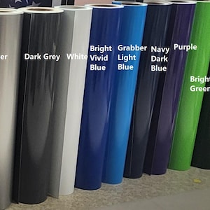 May include: A row of vinyl rolls in various colors labeled Destroyer Light Grey, Silver, Dark Grey, White, Bright Vivid Blue, Grabber Light Blue, Navy Dark Blue, Purple, Bright Green, Dark Polo Green, and Yellow, arranged side by side in a line.