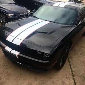 May include: A black two-door coupe featuring a glossy finish and dual white racing stripes with thin red pinstripes running from the front bumper, across the hood, and over the roof. The vehicle has a sculpted hood with air vents.