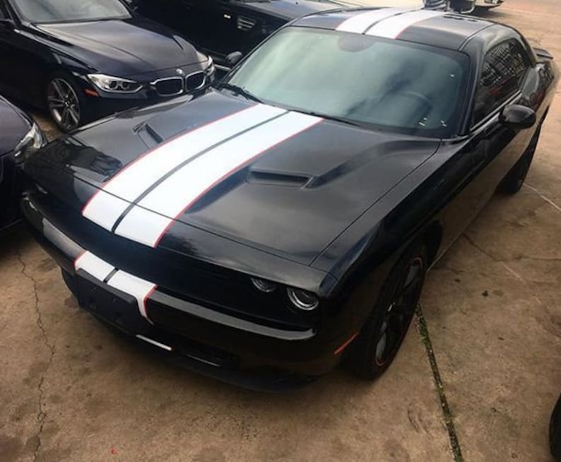 May include: A black two-door coupe featuring a glossy finish and dual white racing stripes with thin red pinstripes running from the front bumper, across the hood, and over the roof. The vehicle has a sculpted hood with air vents.
