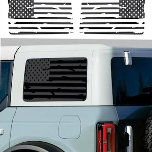 Puede incluir: Calcomanías de ventana con la bandera estadounidense en blanco y negro. Las calcomanías presentan un diseño desgastado de la bandera, con estrellas y rayas. La imagen también muestra las calcomanías aplicadas en la ventana trasera de un vehículo.