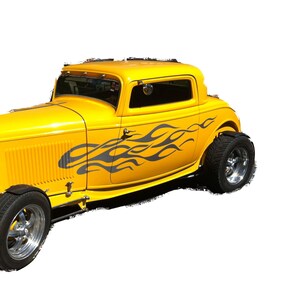 以下が含まれることがあります： 側面に黒い炎が描かれた黄色のビンテージホットロッド。車は黒い内装とクロムメッキのホイールを備えています。