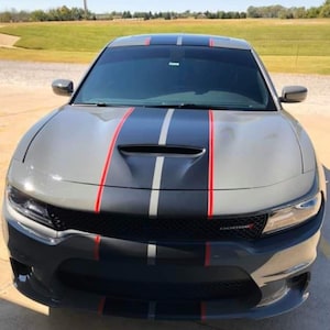 May include: A grey Dodge Charger with black and red racing stripes. The car has a black grille and a black hood scoop.