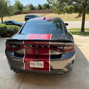 May include: A grey Dodge Charger with a red and white racing stripe down the back. The car has a Texas licence plate that reads "PSC-7936".