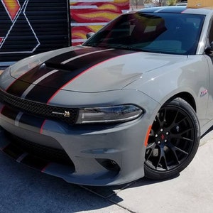 May include: A grey Dodge Charger with black and red racing stripes. The car has black wheels and a black grille.