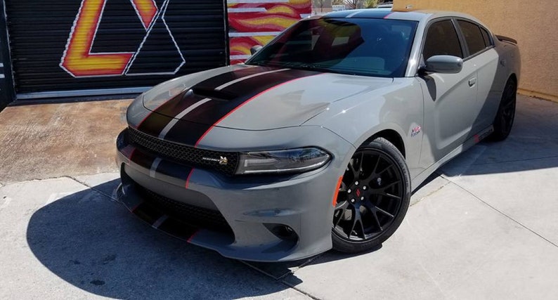 May include: A grey Dodge Charger with black and red racing stripes. The car has black wheels and a black grille.