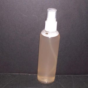 May include: A clear spray bottle with a white top, filled with a light brown liquid. The bottle is transparent, allowing the contents to be visible. The background is a dark gray.