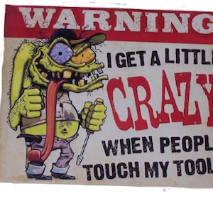 Può includere: Un cartello di avvertimento con un personaggio dei cartoni animati con la faccia verde e una lunga lingua. Il cartello recita "Avviso Divento un po' pazzo quando la gente tocca i miei attrezzi".