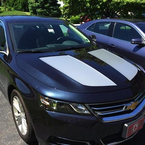 May include: A dark blue saloon car with silver racing stripes on the bonnet. Another blue car is parked behind it. The Chevrolet badge is visible on the front of the car.