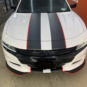 May include: A white Dodge Charger with black and red racing stripes. The car has a black front bumper and a black grille. The number plate is partially obscured.