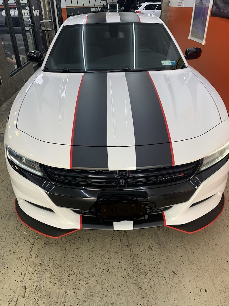 May include: A white Dodge Charger with black and red racing stripes. The car has a black front bumper and a black grille. The number plate is partially obscured.