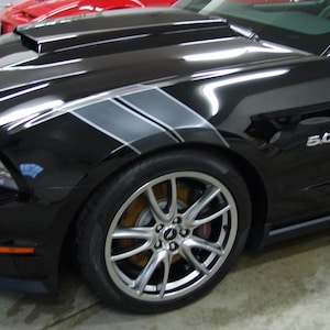 Könnte beinhalten: Schwarzes Sportwagen mit silbernen Felgen und grauen Rennstreifen. Das Auto hat eine Motorhaube und die Nummer "5.0" ist sichtbar. Das Auto steht in einer Garage.