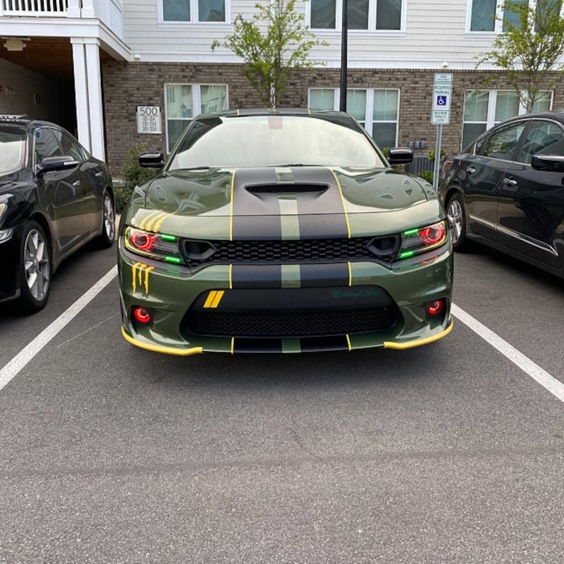 May include: A green Dodge Charger with black racing stripes and yellow accents. The car has green and black camouflage accents on the bonnet and front bumper. The car is parked in a car park.