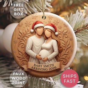 May include: Wooden Christmas ornament with a faux wood print. The ornament features a couple wearing Santa hats, with the woman pregnant. The text "Baby Smith Arriving 2026" is on a banner. The ornament has a gold string for hanging.