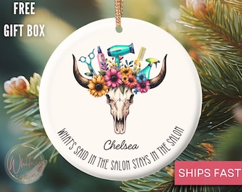 May include: A white ceramic ornament featuring a bull skull adorned with flowers and salon tools. The text reads "WHAT'S SAID IN THE SALON STAYS IN THE SALON" with the name "Chelsea" below. A gold string is attached for hanging.