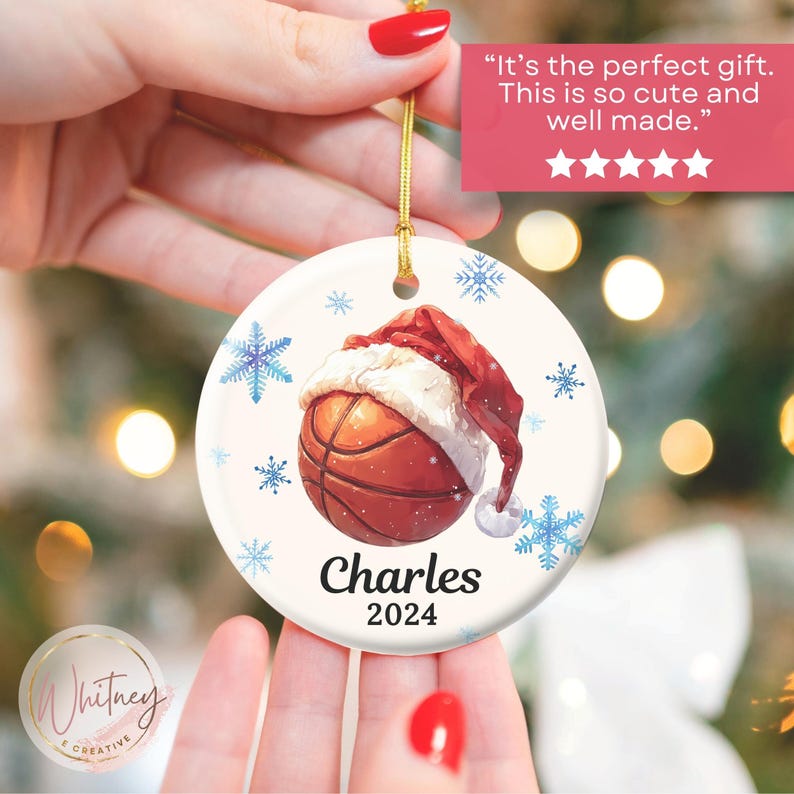 May include: White ceramic Christmas ornament with a basketball wearing a Santa hat. The ornament has blue snowflakes and the text "Charles 2024".