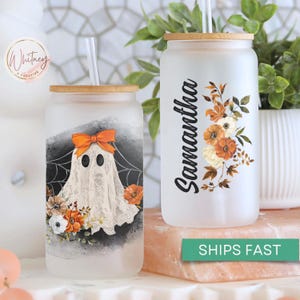 May include: Two frosted glass tumblers with bamboo lids and straws. One tumbler features a ghost with orange and white accents and floral details. The other tumbler has the name Samantha written on it with floral accents.