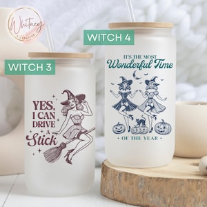 May include: Two frosted glass tumblers with a wood lid and straw. The tumbler on the left has a witch flying on a broomstick with the text "YES, I CAN DRIVE A STICK". The tumbler on the right has two witches dancing with the text "IT'S THE MOST WONDERFUL TIME OF THE YEAR".