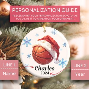 May include: White ceramic Christmas ornament with a basketball wearing a Santa hat. The ornament is decorated with snowflakes and the text "Charles 2024".