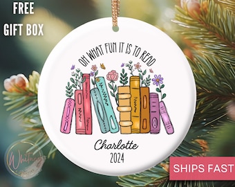 May include: White ceramic Christmas ornament with a colorful illustration of a stack of books with flowers and the text "Oh what fun it is to read". The ornament is personalized with the name "Charlotte" and the year "2024".