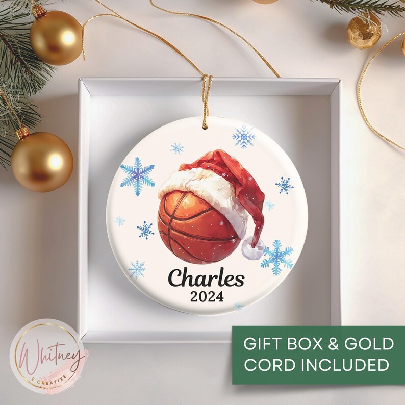 May include: White ceramic Christmas ornament with a basketball wearing a Santa hat. The ornament has blue snowflakes and the text "Charles 2024".