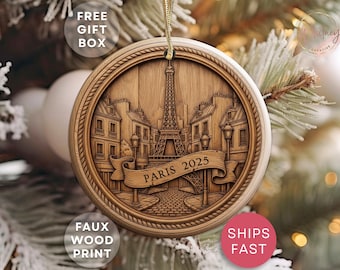 May include: Wooden Christmas ornament with a faux wood print featuring the Eiffel Tower and Parisian buildings. The ornament has a rope-like border and a banner that reads "PARIS 2025". A gold string is attached for hanging.