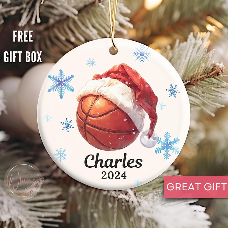 May include: White ceramic Christmas ornament with a basketball wearing a Santa hat. The basketball is orange and brown with white stitching. The ornament has blue snowflakes and the text "Charles 2024".