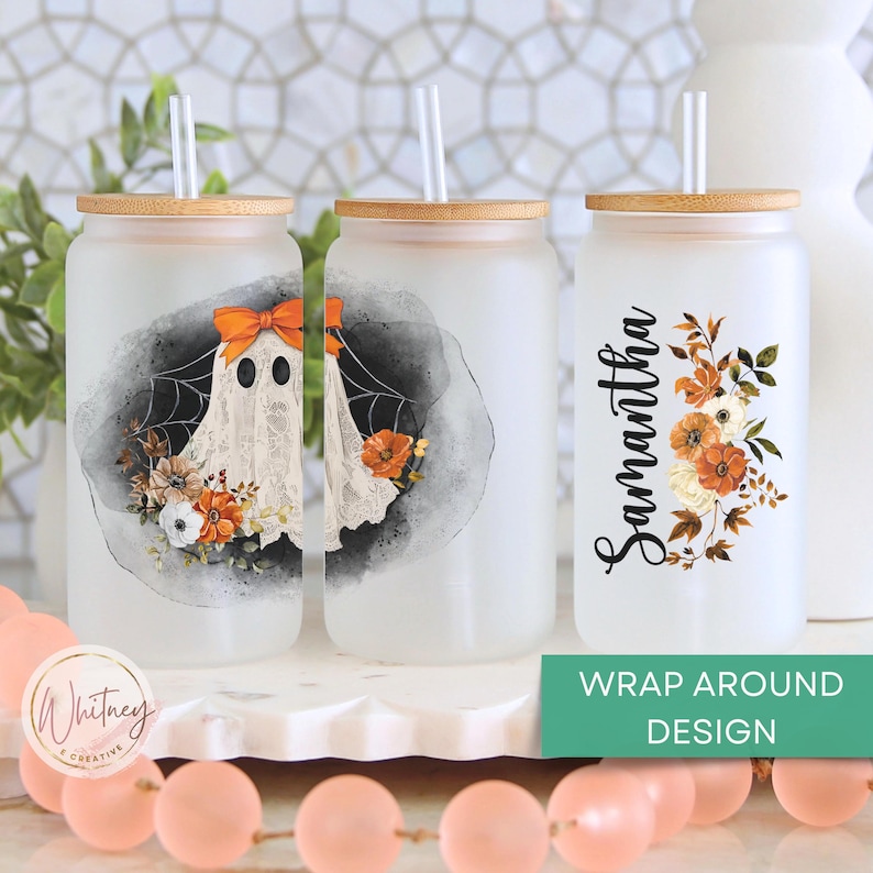 May include: Three frosted glass tumblers with bamboo lids and straws. The tumblers feature a ghost with a spiderweb, a floral design, and the name "Samantha". The tumblers are on a white surface with pink and orange beads.