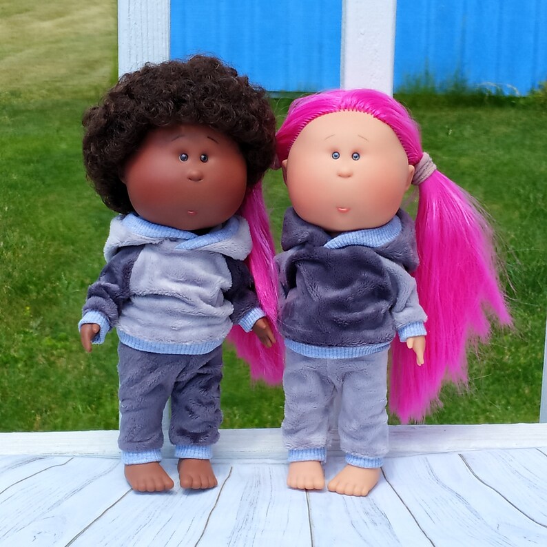 May include: Two plush dolls wearing matching gray and blue pajamas. One doll has brown curly hair and brown eyes, the other doll has long pink hair and blue eyes.